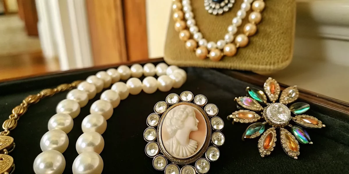 A collection of vintage costume jewelry pieces including rhinestone brooches, pearl necklaces, and enamel earrings displayed on dark velvet